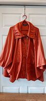 Front view of burnt orange swing cape jacket on hanger showing collar, sleeves, zipper and snaps