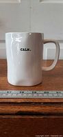 Front view of mug showing "CALM." text and overall shape beside ruler for scale