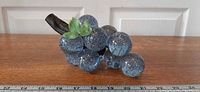 Front three-quarter view of entire grape cluster showing blue lucite grapes, driftwood stem, green leaf, ruler for scale