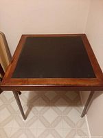 Square wood and leather card table standing on linoleum floor against wall