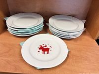 Two stacks of white dinner plates with one Wächtersbach red reindeer plate in front