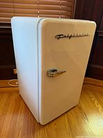 Angled left-front view of white Frigidaire compact fridge showing emblem and handle