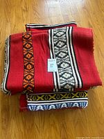 Both red woven blankets folded showing geometric stripes
