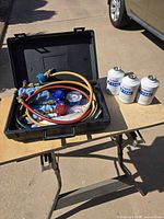 Open case with manifold gauge set and three refrigerant cans on table