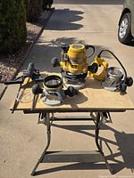 Full kit on folding table: motor in plunge base, fixed base, D-handle base, edge guide, clear sub-base visible