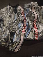 Overall view of jacket and pants displaying metallic fabric and WARNING stripe