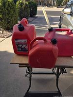 Three red plastic gasoline cans on small table, showing sizes, caps and spout