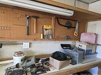 Pegboard with various tools, bench with power tool, cords and supplies