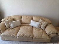 Full view of beige leather couch with four pillows