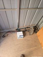 Group of miscellaneous tools on shed floor including grey nozzle, small box, miter gauge, green guide bar