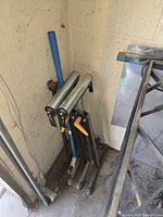 Three folding roller stands leaning in corner showing rollers, legs and adjustment mechanisms