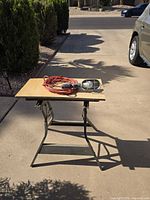 Handheld metal-caged shop light with orange extension cord displayed on small folding table