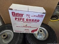 Box of Oatey Pipe Guard resting against two pneumatic wheels