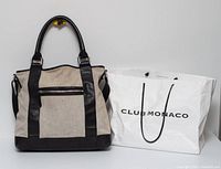 Front view of Club Monaco canvas and leather tote alongside paper shopping bag