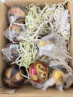 Open box showing eight wrapped ornate ornaments with packing material