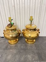 Front view of both gold urn-form lamps showing finish, handles, bases, sockets