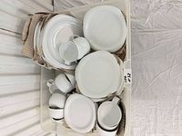Bin containing stacked white porcelain plates, cups, and bowls