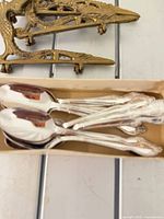 Box with polished silver-plated teaspoons and two brass easels in background