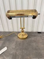 Front view of brass adjustable desk lamp showing shade, arm, base and cord