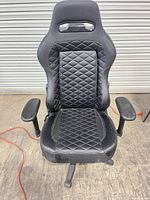 Front view of black G Racer gaming chair showing diamond-stitched seat and adjustable armrests