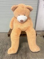Front view of giant tan IKASA teddy bear seated on table