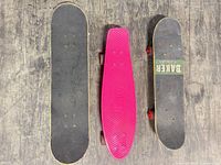 Three boards top sides: two wood street decks with black grip and pink plastic cruiser