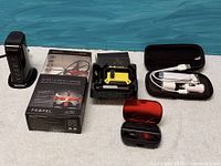 Group shot of boxed drone, charging tower, jump starter, earbuds, cable kit