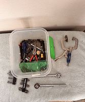Overview of clear tub with assorted tools, locking C-clamp pliers, ratchets, green scraper and multi-socket wrench