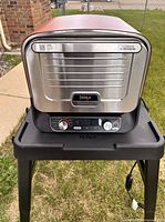 Front view of Ninja Woodfire oven on stand showing control panel and logo
