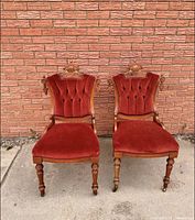 Front view of two Victorian red velvet side chairs against brick wall