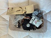 Plastic bin holding assorted jewellery and hair accessories including carded earrings and fabric pieces