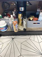 Overall view under sink showing baskets with assorted cleaning products, copper scrubbers, sponges