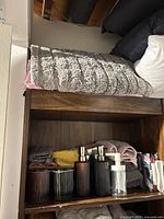 Upper shelf with folded gray striped throw, pillows, towels, ribbed plastic dispensers in front