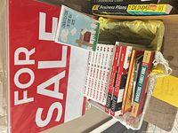 Stack of real estate books, For Sale sign, greeting card visible