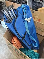 Box containing blue chair in sleeve, visible aluminum frame, teal and orange sacks