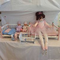 Overall view showing two wooden doll beds, one wooden cradle, large rag doll, two baby dolls, bedding, bottle and plush toy