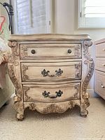 Front view showing three drawers, ornate carvings, metal hardware