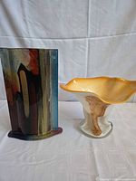 Tall multicolor art glass vase beside ruffled pedestal bowl