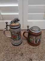 Front view of both steins showing size difference, decoration and pewter lids