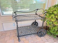 Full view of two-tier cast aluminum patio bar cart against wall