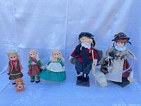 Group shot of five dolls and bear on white backdrop