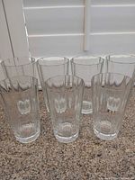 Front view of six of the seven clear glass tumblers showing height, shape, and condition