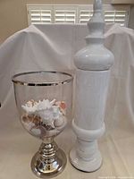 Glass urn with seashells and tall white lidded jar side by side