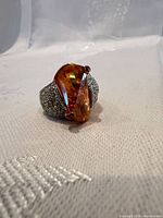 Front view of ring showing pear orange glass center stone and pavé shoulders