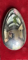 Full view of egg-shaped paperweight on red background showing engraving and reflective surface