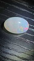 Oval cabochon opal showing rainbow play of color on black background
