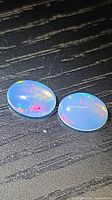 Both oval cabochon opals showing play-of-colour on dark surface