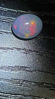 Oval cabochon opal showing multicolor flashes on black background