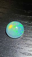 Round cabochon opal on black background showing green and orange fire