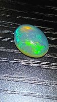 Top view of oval crystal opal showing vivid green and blue play-of-color